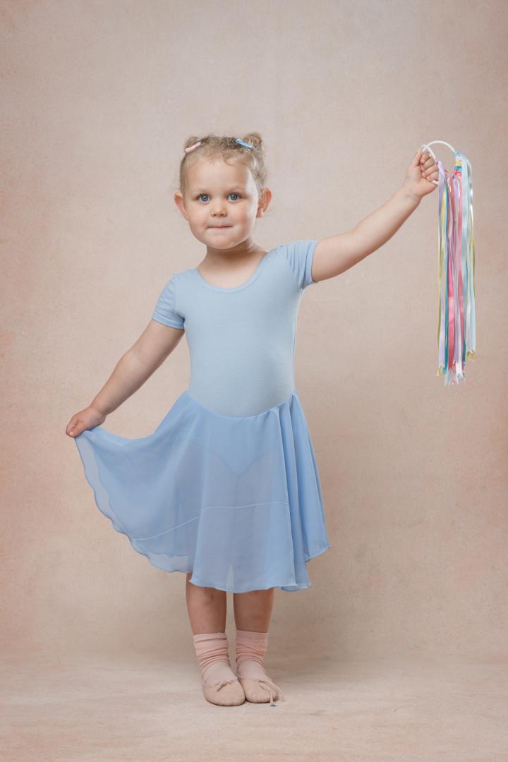 A young girl in a blue ballet outfit holding colorful ribbons, smiling gently.