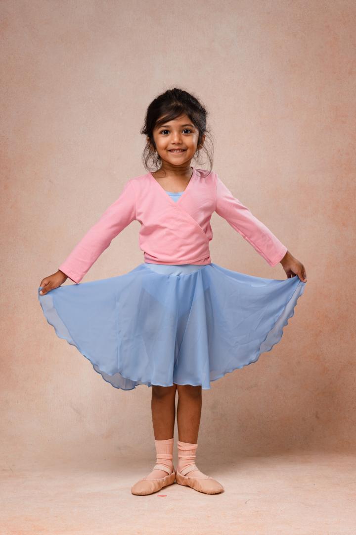 A young girl in a pink and blue ballet outfit smiling and holding her skirt out to the sides.